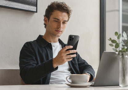 Man using a smartphone at a desk with a laptop and coffee cup